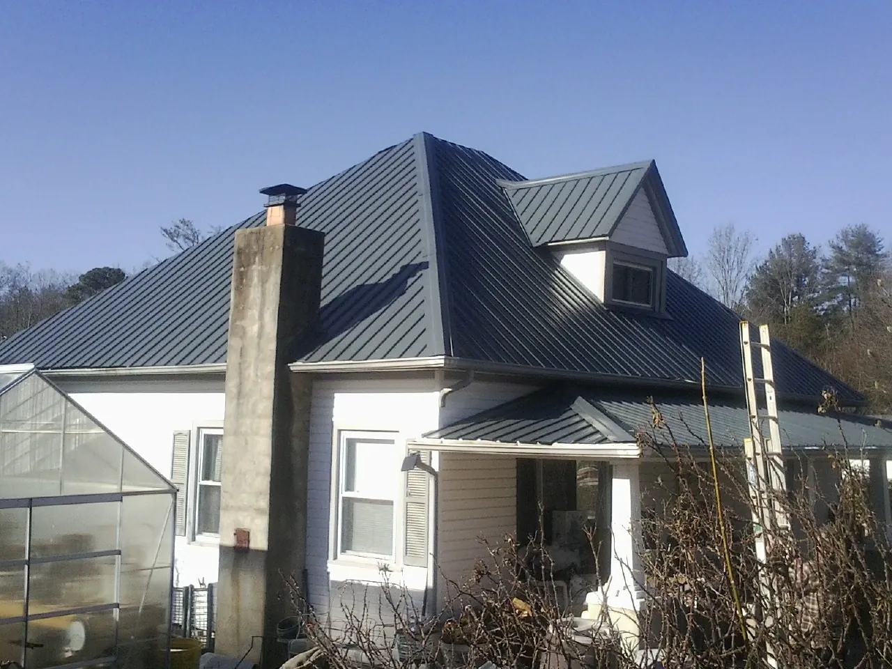 Dark blue standing seam metal roof on a white farmhouse with dormer — Slate & Tile Roof Repair by Roofing Brothers in Rice