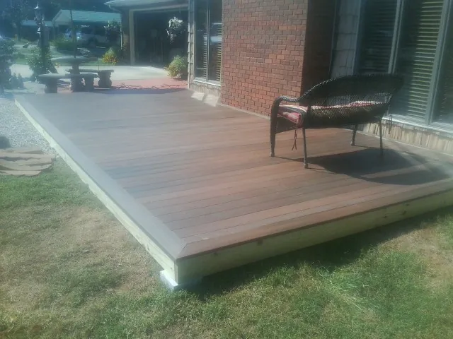 New wood deck and wicker chair beside a brick house in Rice
