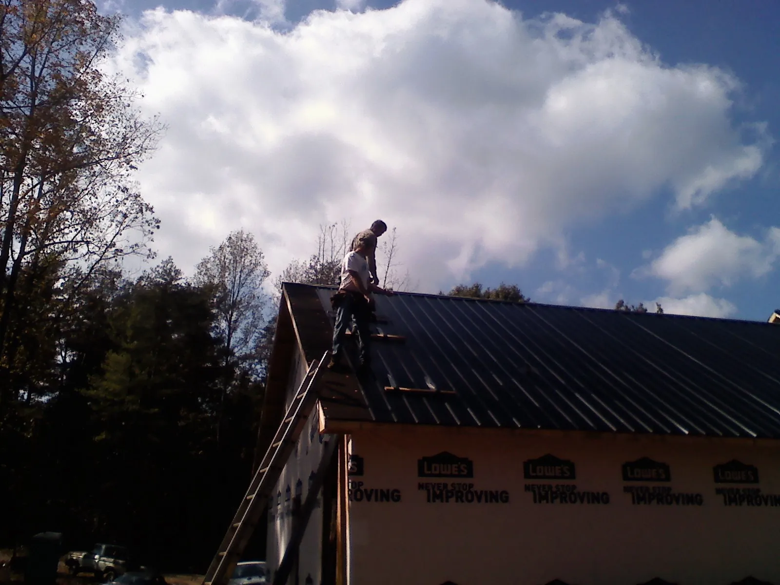 Roofer fastening dark metal panels high against a cloudy sky, from a Roof Inspection job in Rice